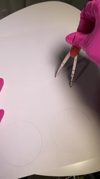 Vertical top-down video showing a compass drawing circles on white paper in a close-up process shot.