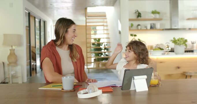 Mother and daughter high-fiving, daughter using tablet and drawing at kitchen table for learning
