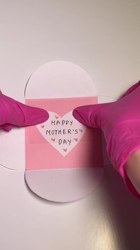 Vertical top-down video of a greeting card with &ldquo;Happy Mother&rsquo;s Day&rdquo; text being sealed with transparent tape, festive composition, soft natural lighting, clean DIY crafting process.