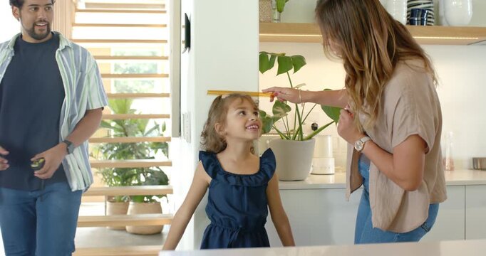 Diverse family measuring height, man coming with yellow tape, woman marking wall tracking growth