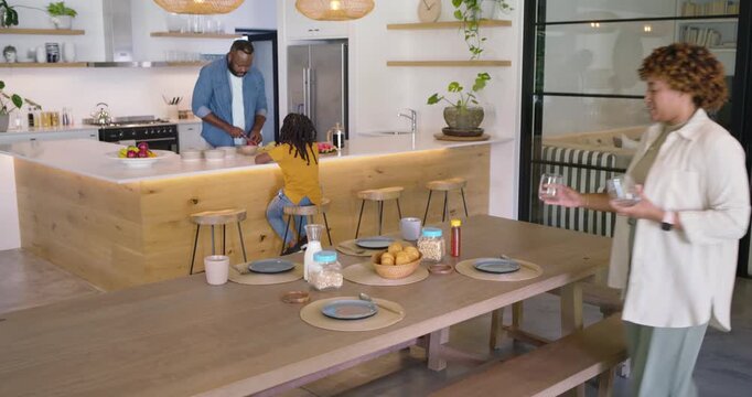 African family preparing breakfast, mother entering with glass, father slicing, son placing juice