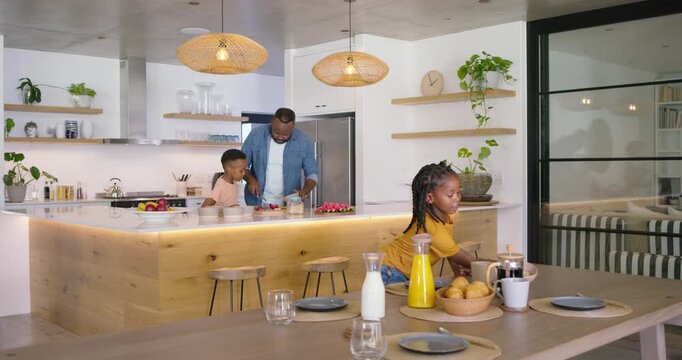 African American family preparing breakfast in modern kitchen, mother entering carrying cereal