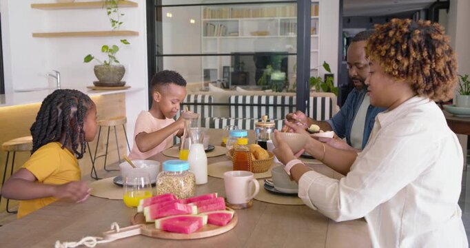 African American family having breakfast at table father reaching urging parents giving kids cereal