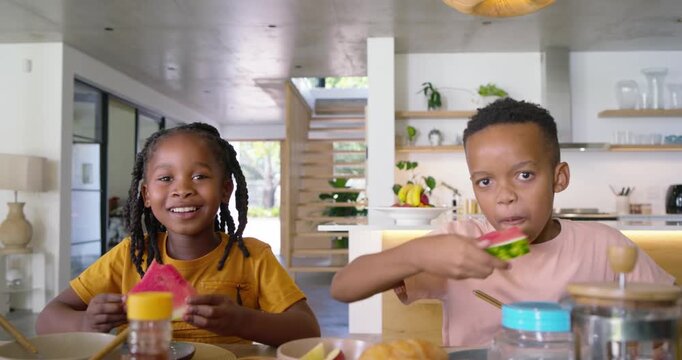 African American school-age siblings spotting watermelon, reaching, eating for breakfast in kitchen