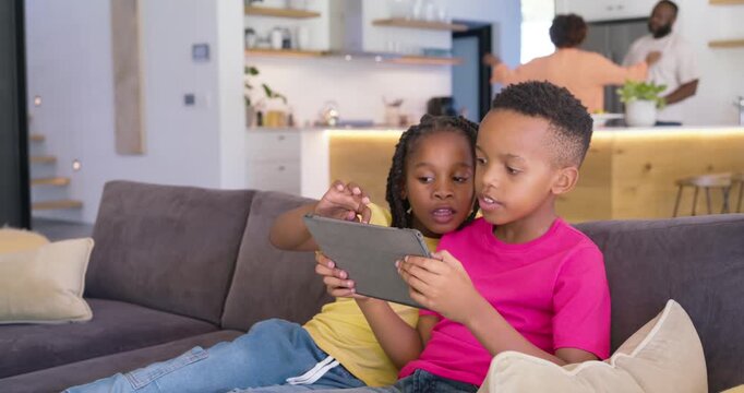 African American siblings sitting couch at home, girl pointing tablet, boy swiping, showing screen