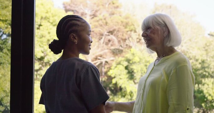 Caregiver in scrubs entering left guiding senior at glass door inviting garden view clasping hands