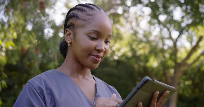 African American woman in gray scrub top tapping tablet replying to message outdoors