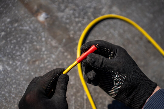 Gloved hands placing a red heat shrink tube over a yellow electrical cable beside a kit of colored shrink tubing outdoors.