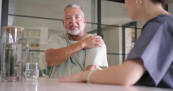 African American man with glass rubbing shoulder and discussing pain with Asian nurse at counter