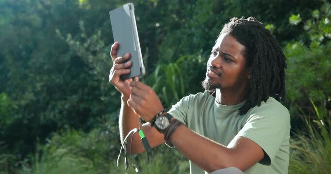 Seeing solar panel on grass African American man lifting tablet plugging green tape cable to charge