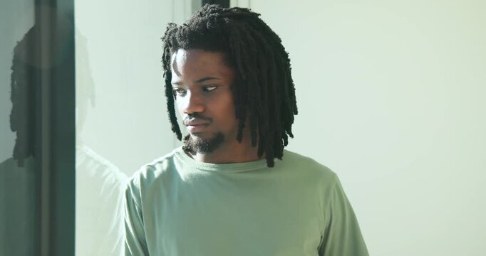 African American man by glass door in lightgreen long-sleeve shirt, tilting into sunlit reflection