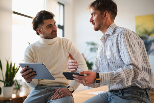Two men are engaged in a discussion while holding digital tablets, suggesting a collaborative work session or a casual meeting.