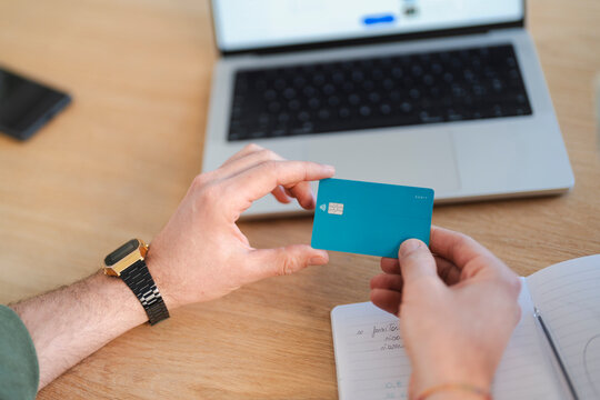 A person holds a debit card near a laptop and notebook, suggesting online banking or financial planning.