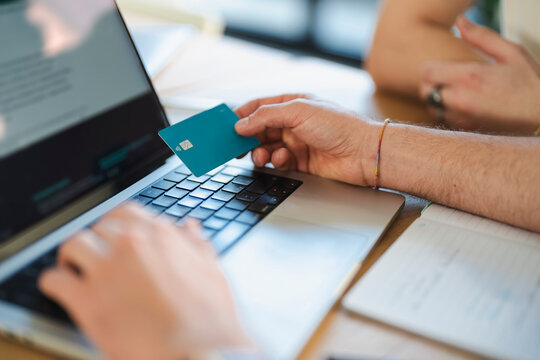 A person uses a credit card to make an online purchase on a laptop, with a notebook open nearby.