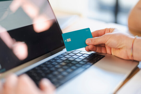 A person holds a debit card near a laptop, ready to make an online payment.