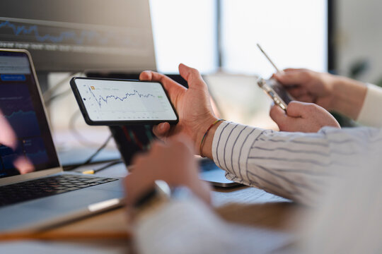 Two people analyze financial data on a laptop and smartphone, showing stock market charts and graphs.