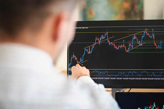 A man in a white shirt analyzes a financial chart on a computer screen, pointing at the data with his finger.
