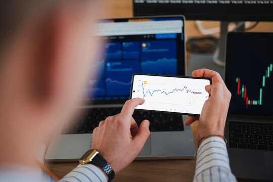 A person analyzes financial charts on a smartphone and laptops, indicating a focus on market trends and investment strategies.