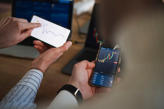 A person analyzes financial charts on a smartphone and laptop, indicating a focus on market trends and investment strategies.