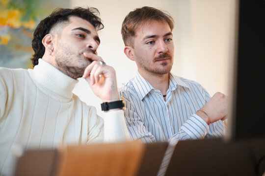 Two men are collaborating on a project, looking intently at a computer screen. They are engaged in discussion and problem-solving.