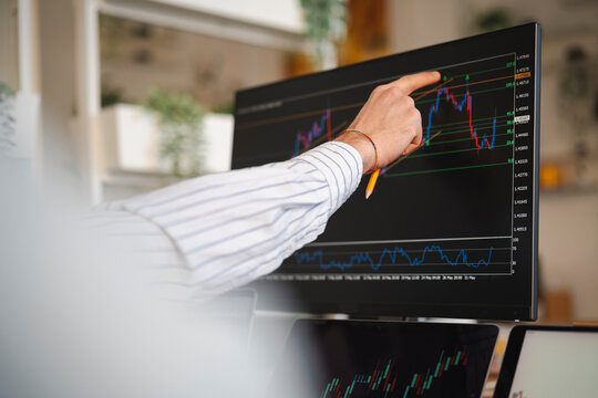 A person's hand points to a financial chart on a computer screen, analyzing market data.
