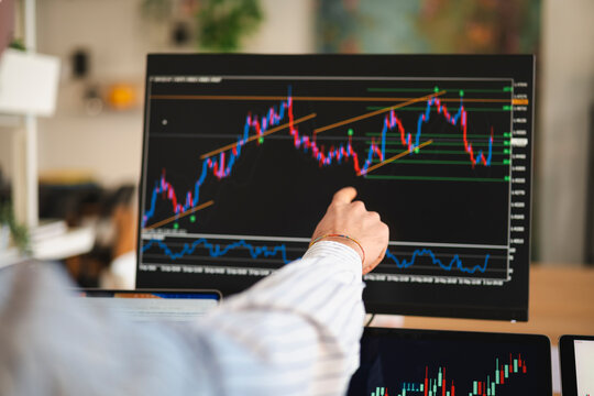 A person's hand points to a financial chart on a computer screen, analyzing market trends and data.