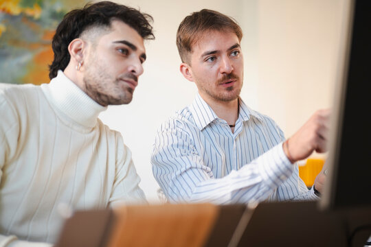 Two men collaborate on a project, one pointing at a computer screen while the other listens attentively.