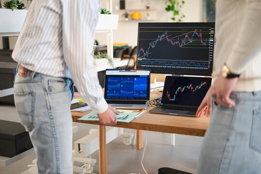 Two people analyze financial charts on multiple screens, discussing market trends and investment strategies at a modern desk.