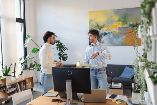 Two men are in a modern office, discussing documents and looking at a computer screen.