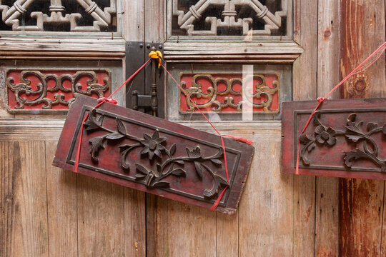 Close up of an antique Chinese wooden door with intricately carved floral wooden panels hanging by red strings