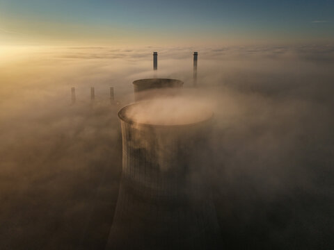 Aerial view of the RWE Clauscentrale power plant cooling towers and chimneys emerging from a thick layer of morning fog at sunrise in Maasbracht, Limburg, Netherlands.