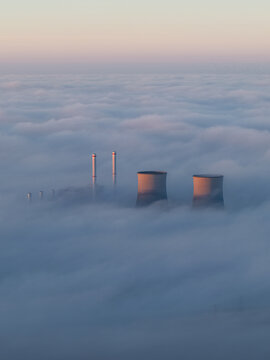 Aerial view of RWE Clauscentrale power plant with cooling towers and chimneys emerging from a thick layer of fog under a soft morning sky Maasbracht, Limburg, Netherlands.