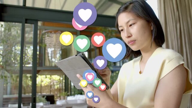 Woman tapping tablet in lounge generating social hearts forming column, obscuring face, reacting