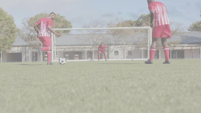 Left outfield player striking ball toward goal, goalkeeper diving right to save during sports drill