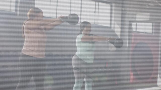 Two women training together in gym, hip driving kettlebells upward, performing reps for strength