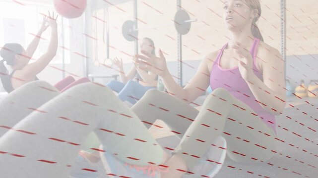 Woman in purple bracing, receiving and passing red medicine balls, leading class doing core sit-ups