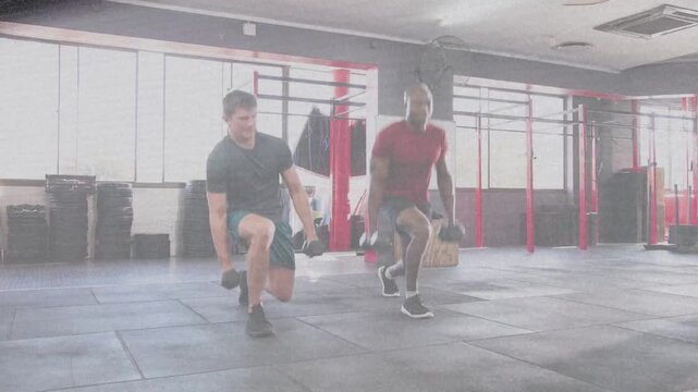 Two men starting side-by-side, doing in-sync dumbbell walking lunges across gym mat for strength