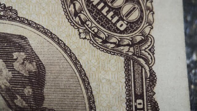 The edge design detail of an antique Hungarian 100 million pengo banknote from 1946. The footage highlights ornate border engraving, denomination ornament, and fine linework.