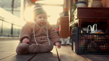Baby crawling in bear teddy fleece coat and striped beanie hat smiling while moving on wooden floor, toddler exploring environment playfully during winter afternoon © Marco