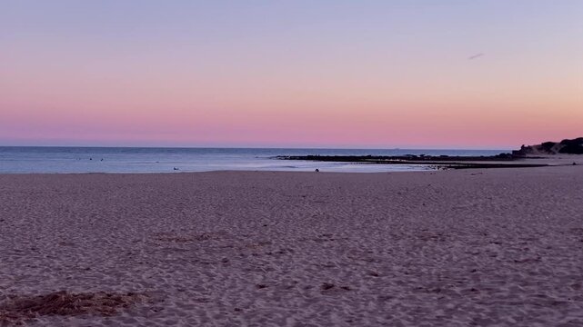 Wide angle view of a quiet beach with vibrant pastel sky gradient during sunset, showing calm ocean and distant shore
