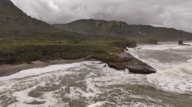 Drone view of rugged coastline near Truman Track on West Coast of New Zealand&rsquo;s South Island, featuring crashing waves, rocky shorelines, lush cliffs and dramatic stormy skies.