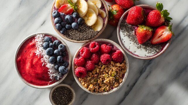 Close-up of four colorful smoothie bowls, laden with fresh fruits, granola, and chia seeds, atop a marble surface