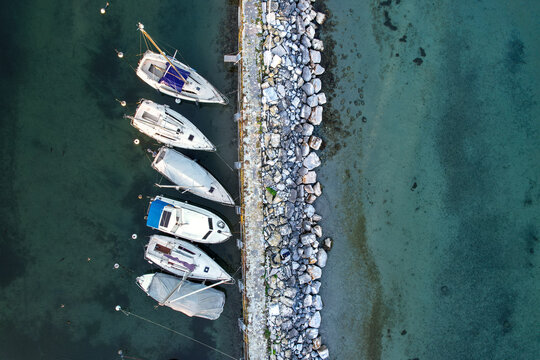 Aerial view of sailboats moored along a stone pier in the clear turquoise waters of Lake Geneva in Morges, Vaud, Switzerland.