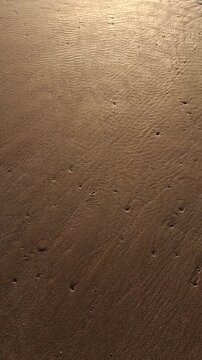 Handheld point of view of walking on wet sand at the beach during golden hour sunrise with organic textures and natural light