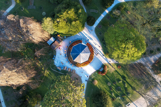 Aerial view of the octagonal pavilion in Parc de l'Independance surrounded by blooming tulip beds, lush green trees and people walking on paths in Morges, Vaud, Switzerland.