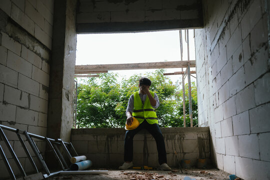 Tired construction worker resting at a building site while holding a safety helmet, representing workplace stress, fatigue, and construction industry challenges.