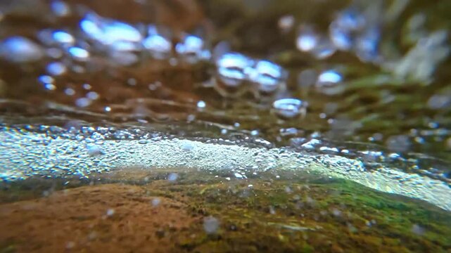 Split level view of moving water surface with bubbles. Macro shot of the interface between air and water in a flowing mountain stream.