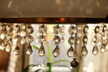 Naklejka premium Close-up of hanging crystal prisms on a vintage chandelier, bathed in warm sunlight. The faceted drops sparkle, creating a mesmerizing play of light and rainbow reflections. The soft glow and intricat