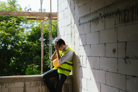 Tired construction worker resting at a building site while holding a safety helmet, representing workplace stress, fatigue, and construction industry challenges.