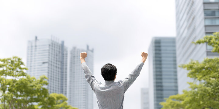 Young Asian man raises his arms to meet challenges against the backdrop of high-rise buildings in the city